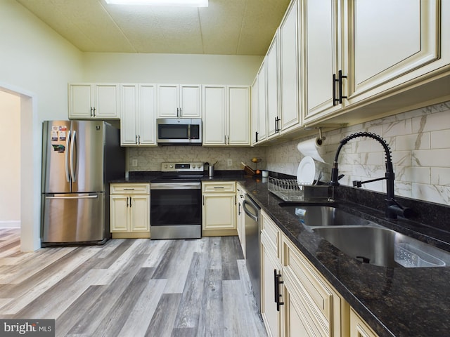 kitchen with sink, appliances with stainless steel finishes, dark stone counters, light hardwood / wood-style floors, and backsplash