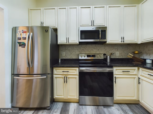 kitchen featuring stainless steel appliances, light hardwood / wood-style floors, decorative backsplash, and dark stone counters