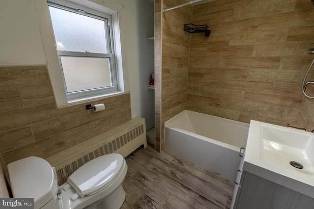 full bathroom featuring radiator, vanity, tiled shower / bath combo, hardwood / wood-style floors, and toilet