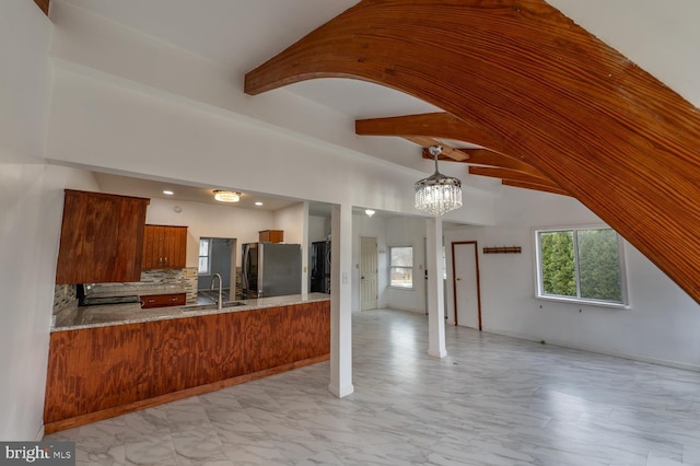 kitchen with kitchen peninsula, stainless steel fridge, backsplash, sink, and pendant lighting