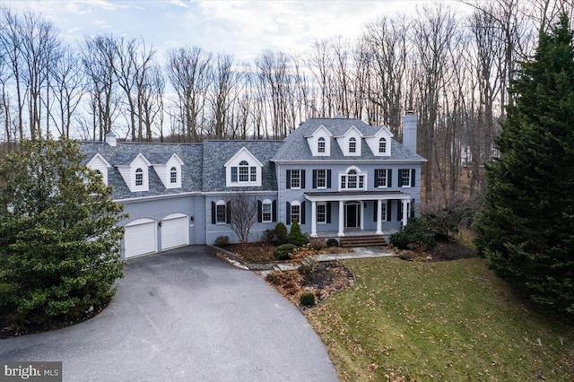 view of front of property with driveway, covered porch, a front yard, a garage, and a chimney