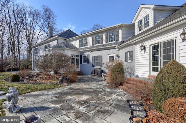 exterior space featuring brick siding, a chimney, and a patio