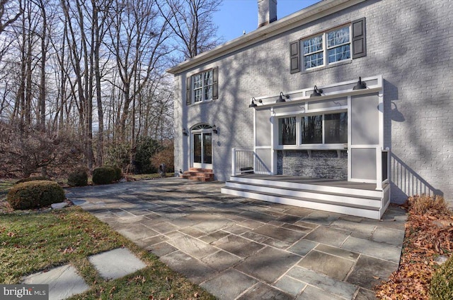 rear view of property with entry steps, brick siding, a patio, and a chimney