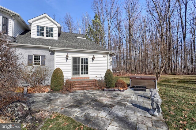 rear view of house with a patio, brick siding, a shingled roof, a lawn, and a hot tub