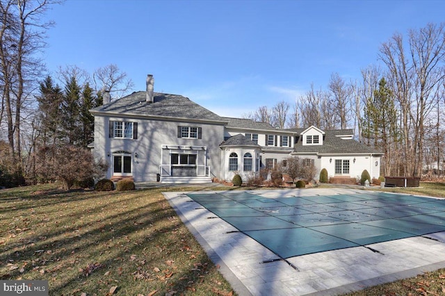 rear view of property featuring a covered pool, a chimney, and a yard