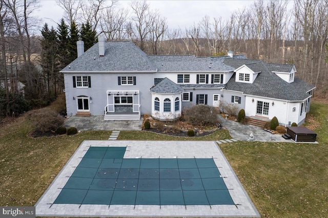 back of property featuring a lawn, a patio, a covered pool, a chimney, and roof with shingles