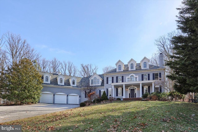 colonial home with covered porch, aphalt driveway, a front yard, and an attached garage