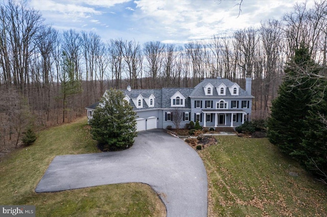 view of front of property featuring aphalt driveway, an attached garage, covered porch, a front lawn, and a chimney