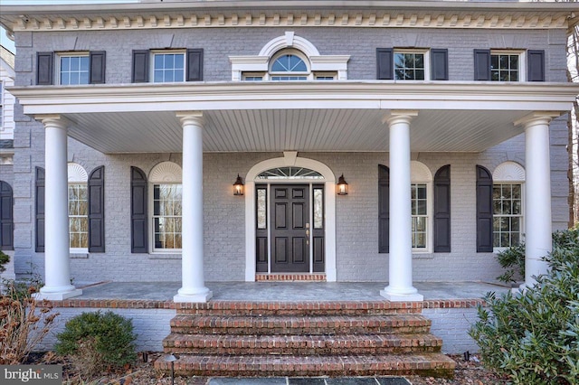 view of exterior entry featuring brick siding and a porch