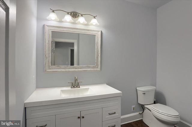 bathroom featuring toilet, baseboards, wood finished floors, and vanity