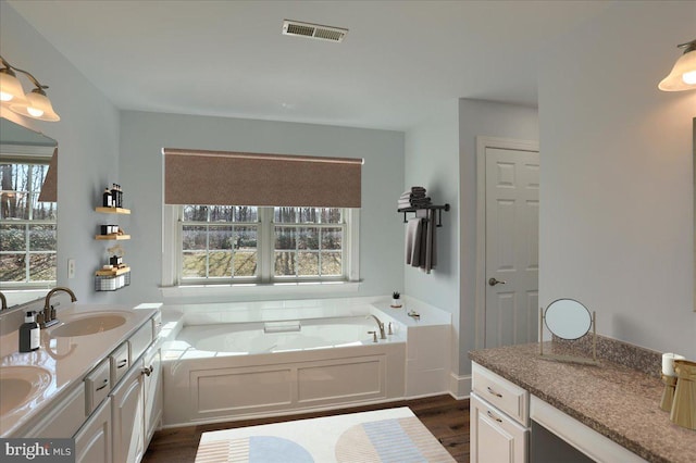 full bathroom with double vanity, visible vents, wood finished floors, a sink, and a bath