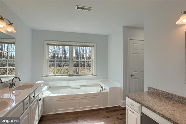 full bathroom with double vanity, visible vents, wood finished floors, a sink, and a bath