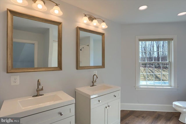 bathroom with wood finished floors, two vanities, a sink, and baseboards