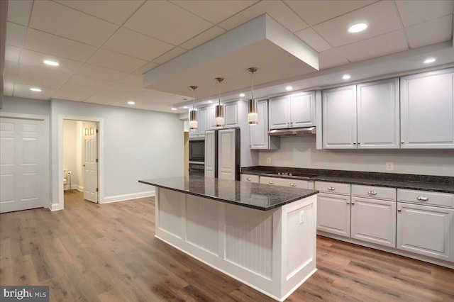 kitchen featuring a center island, decorative light fixtures, wood finished floors, under cabinet range hood, and black appliances