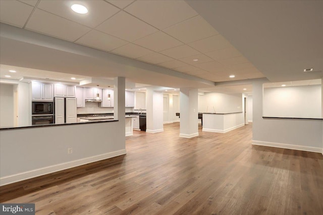 unfurnished living room featuring dark wood-type flooring, recessed lighting, a paneled ceiling, and baseboards