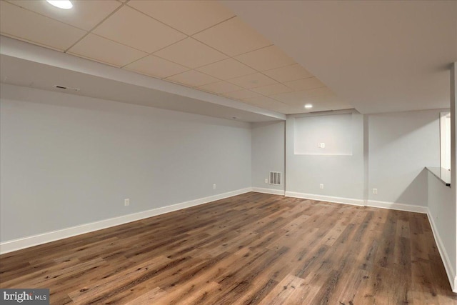 finished below grade area with baseboards, visible vents, a drop ceiling, and wood finished floors