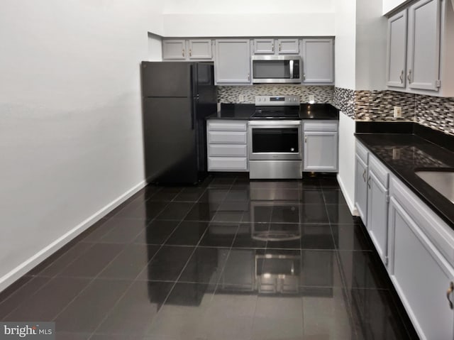 kitchen with dark tile patterned floors, stainless steel appliances, tasteful backsplash, and gray cabinetry