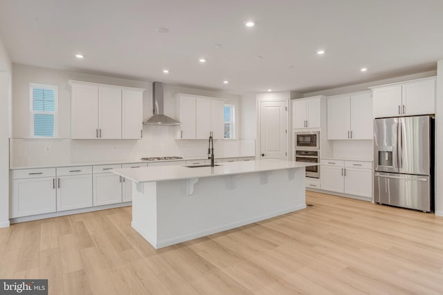 kitchen with white cabinets, sink, wall chimney exhaust hood, an island with sink, and stainless steel appliances