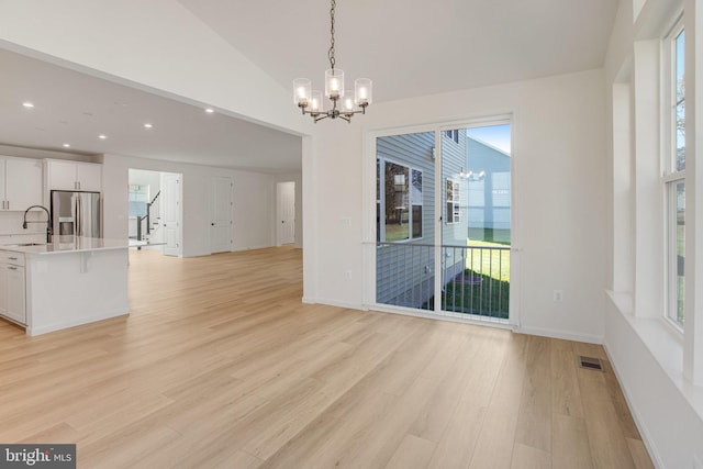 unfurnished dining area featuring light wood-type flooring, an inviting chandelier, and a healthy amount of sunlight