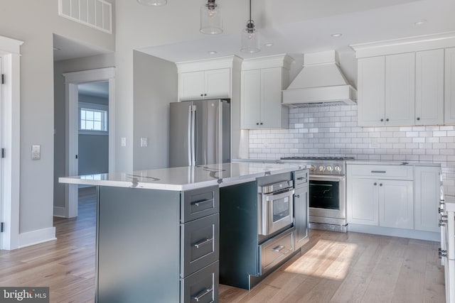 kitchen featuring white cabinets, appliances with stainless steel finishes, premium range hood, and a kitchen island