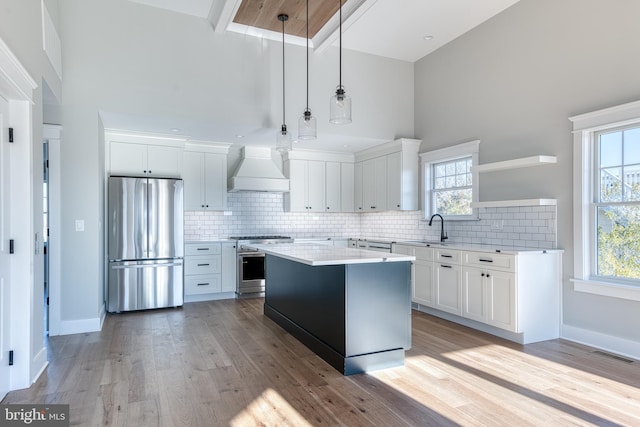 kitchen featuring white cabinetry, hanging light fixtures, a towering ceiling, appliances with stainless steel finishes, and custom exhaust hood