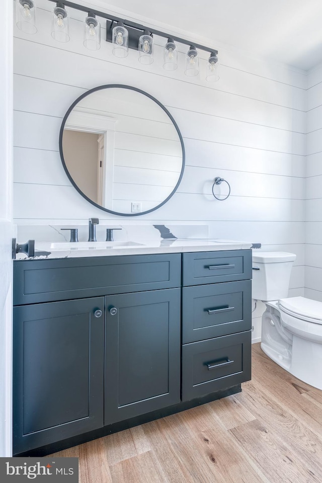 bathroom with wooden walls, hardwood / wood-style floors, vanity, and toilet