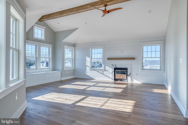 unfurnished living room with ceiling fan, lofted ceiling with beams, wood walls, and light wood-type flooring