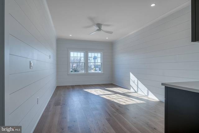 spare room with crown molding, ceiling fan, wooden walls, and light hardwood / wood-style floors