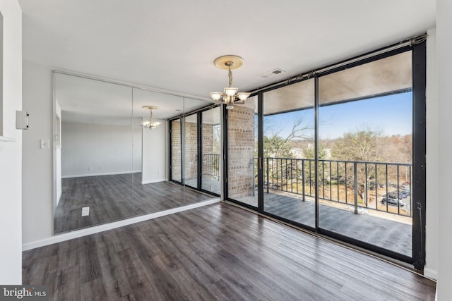 empty room with a notable chandelier, a wall of windows, and dark wood-type flooring