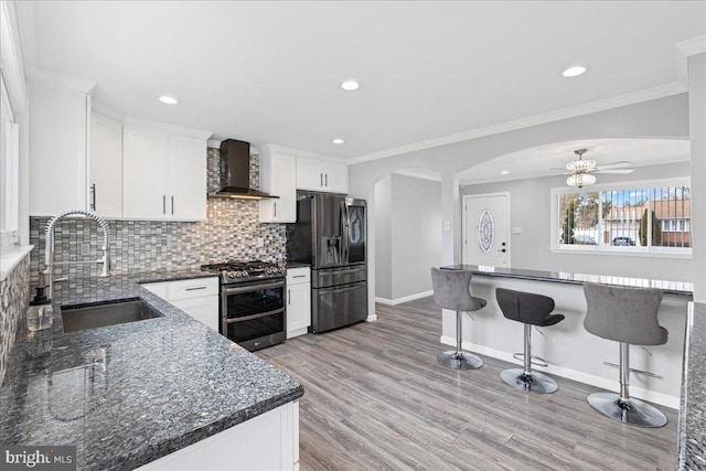 kitchen with sink, white cabinets, backsplash, stainless steel appliances, and wall chimney exhaust hood