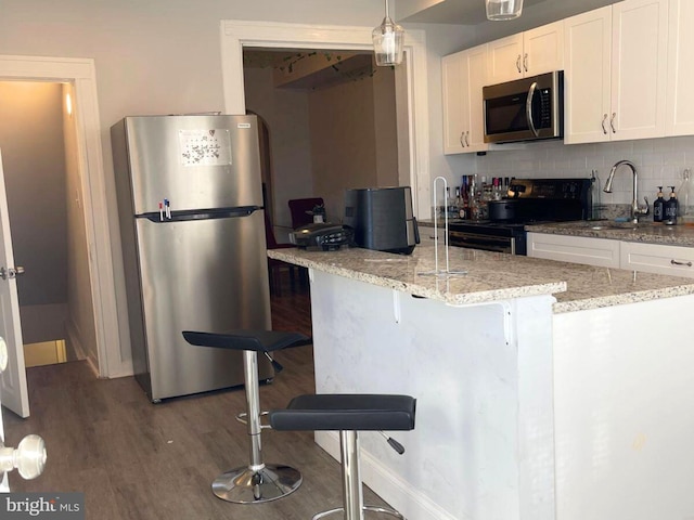 kitchen featuring sink, a breakfast bar, appliances with stainless steel finishes, hanging light fixtures, and white cabinets