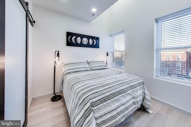 bedroom with a barn door, light wood-type flooring, and multiple windows