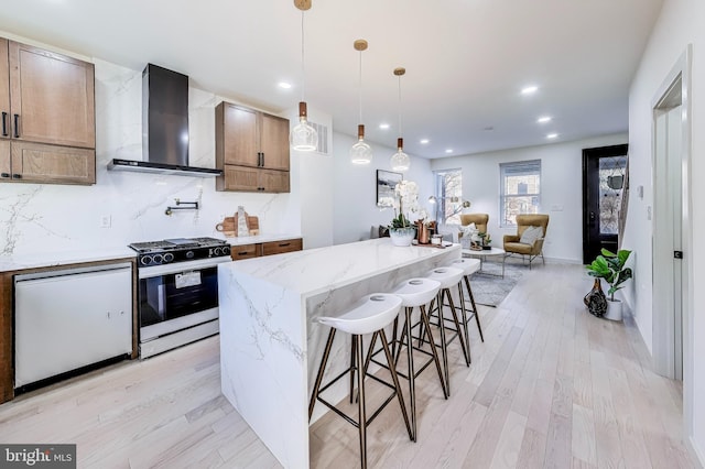 kitchen with range with gas stovetop, wall chimney exhaust hood, light wood-type flooring, and decorative light fixtures