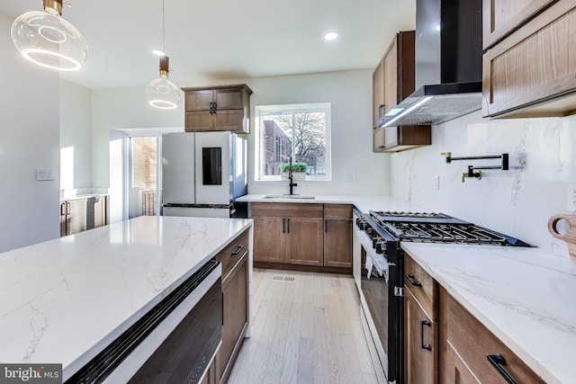 kitchen featuring wall chimney exhaust hood, white refrigerator, high end stove, decorative light fixtures, and light wood-type flooring