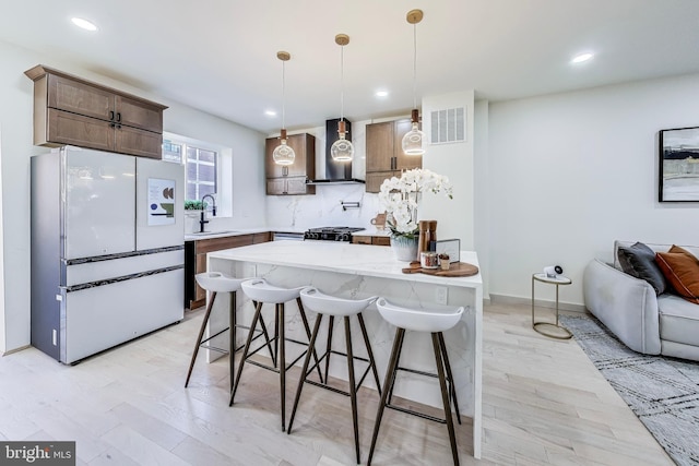 kitchen with sink, wall chimney exhaust hood, white fridge, pendant lighting, and a kitchen island