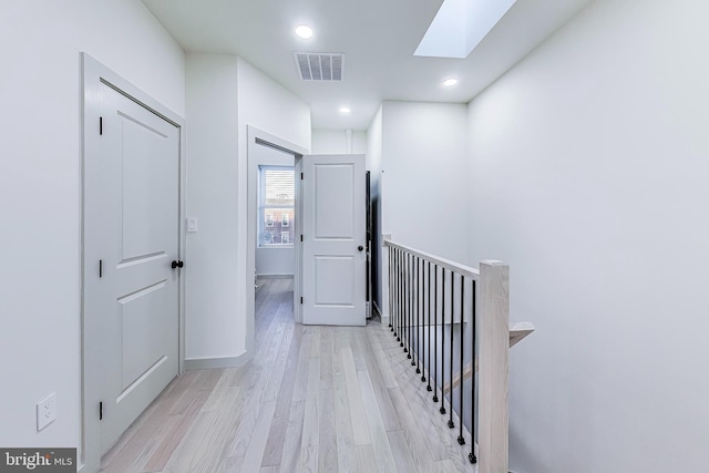 corridor with light wood-type flooring and a skylight