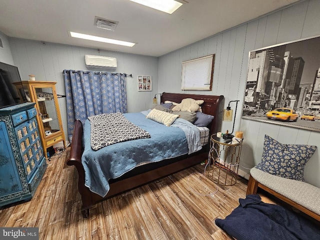 bedroom featuring hardwood / wood-style floors, a wall unit AC, and wooden walls