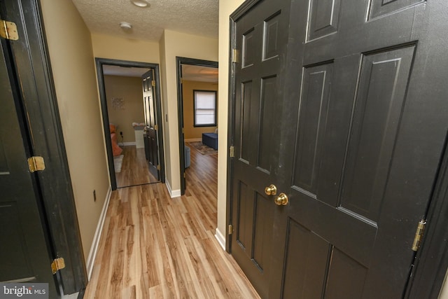 hallway with light wood-type flooring and a textured ceiling