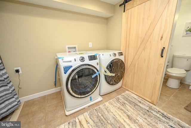 clothes washing area with light tile patterned floors, a barn door, and washing machine and dryer