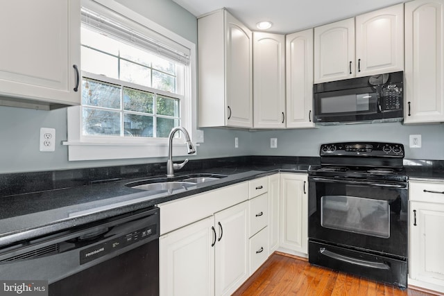 kitchen with black appliances, sink, light hardwood / wood-style flooring, dark stone countertops, and white cabinetry