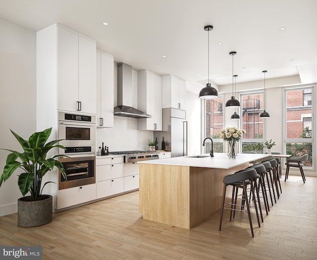 kitchen featuring a center island with sink, wall chimney exhaust hood, white cabinetry, and light hardwood / wood-style flooring