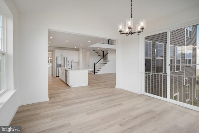 unfurnished dining area featuring sink, plenty of natural light, an inviting chandelier, and light wood-type flooring