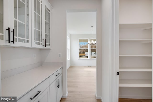 bar featuring a chandelier, white cabinetry, hanging light fixtures, and light hardwood / wood-style flooring