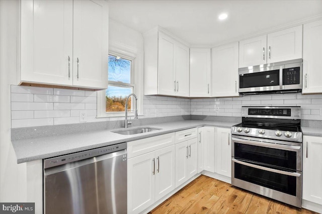 kitchen with white cabinets, sink, appliances with stainless steel finishes, and light hardwood / wood-style flooring