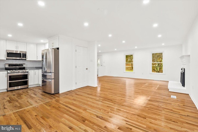 kitchen with tasteful backsplash, white cabinetry, light wood-type flooring, and appliances with stainless steel finishes