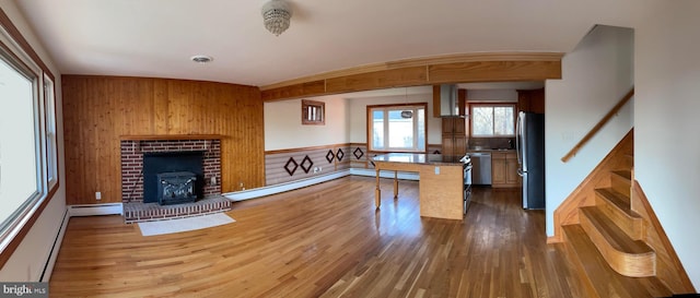 kitchen with wood walls, kitchen peninsula, baseboard heating, and appliances with stainless steel finishes