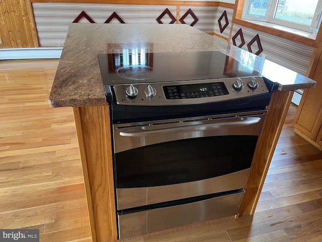 interior details featuring stainless steel electric range oven, a center island, dark stone counters, and light wood-type flooring