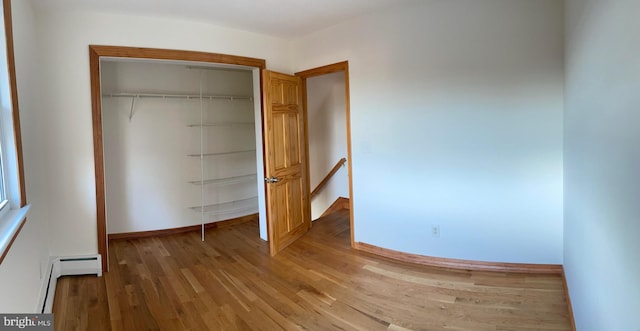 unfurnished bedroom featuring baseboard heating, a closet, and hardwood / wood-style flooring