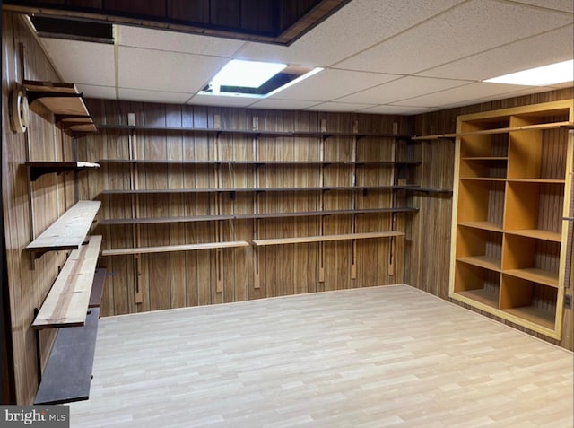 basement with a drop ceiling, wooden walls, and light hardwood / wood-style flooring