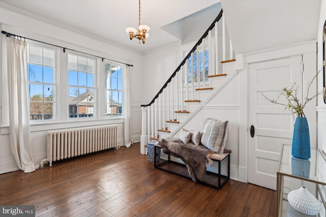 foyer with radiator heating unit, ornamental molding, dark wood-type flooring, and a chandelier